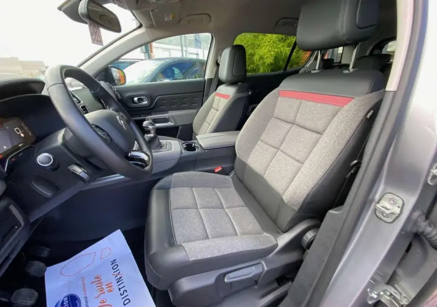 Vue intérieure côté conducteur du Citroën C5 Aircross gris Artense, sièges tissu gris avec bande rouge et volant cuir.