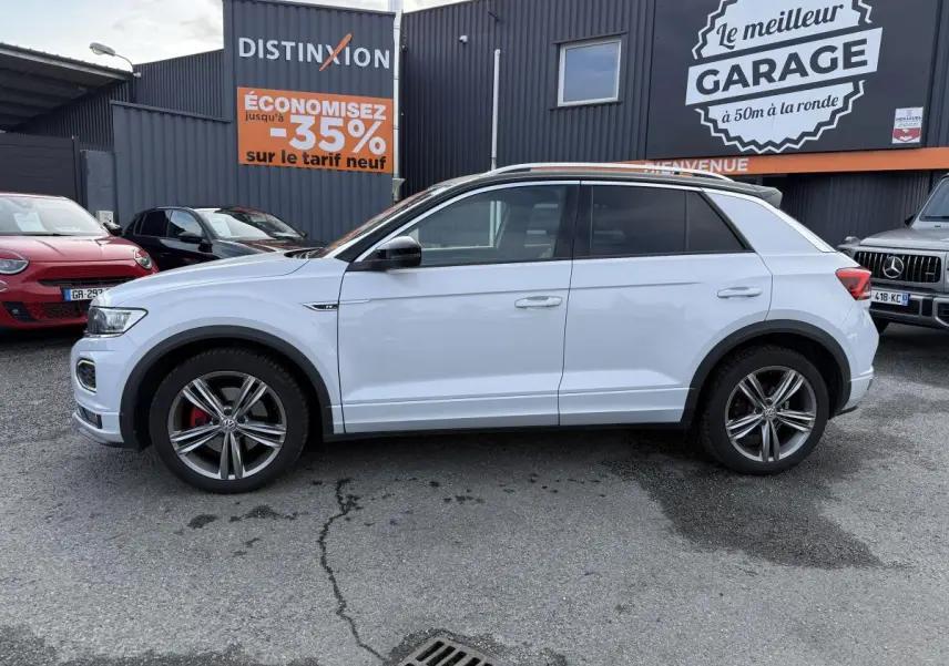 Volkswagen T-Roc blanc vue de profil côté gauche, jantes alliage 18 pouces et détails R-Line visibles.