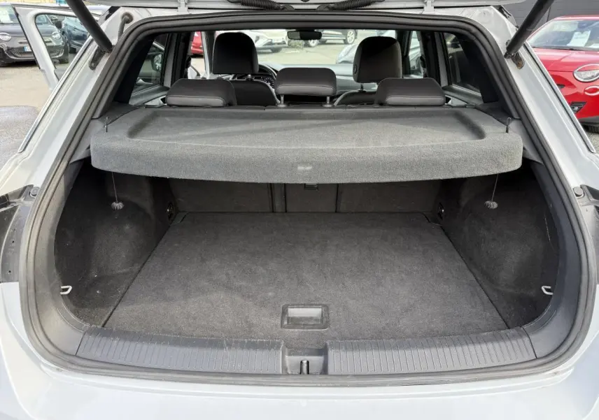 Coffre ouvert vu de l'arrière d'un Volkswagen T-Roc gris avec cache-bagages et sièges arrière visibles.
