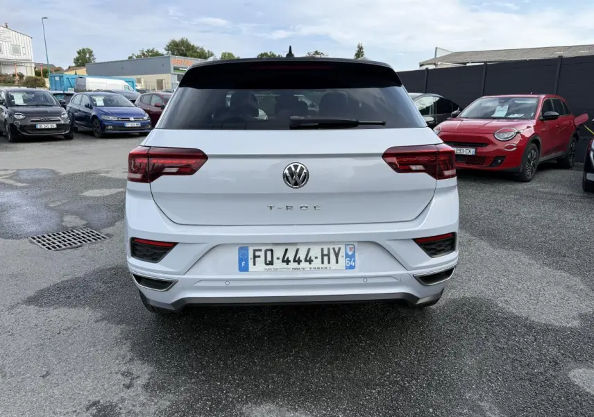 Vue arrière d'un Volkswagen T-Roc blanc avec toit noir et feux arrière LED, garé sur un parking extérieur.