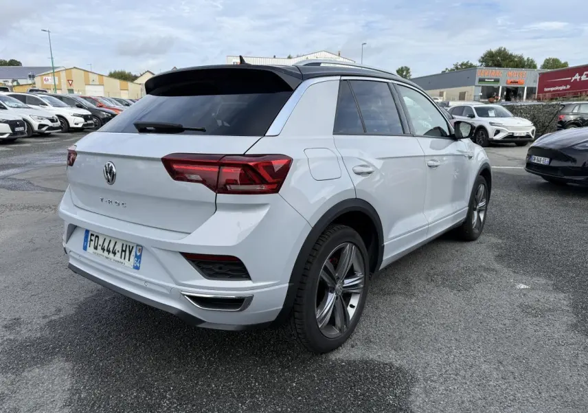 Volkswagen T-Roc blanc vue 3/4 arrière droit avec toit noir et jantes alliage sur parking.