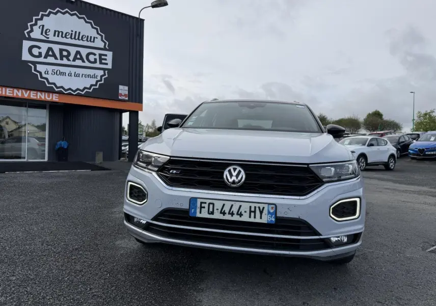 Vue frontale d'un Volkswagen T-Roc gris avec calandre noire et feux LED en forme de losange allumés.