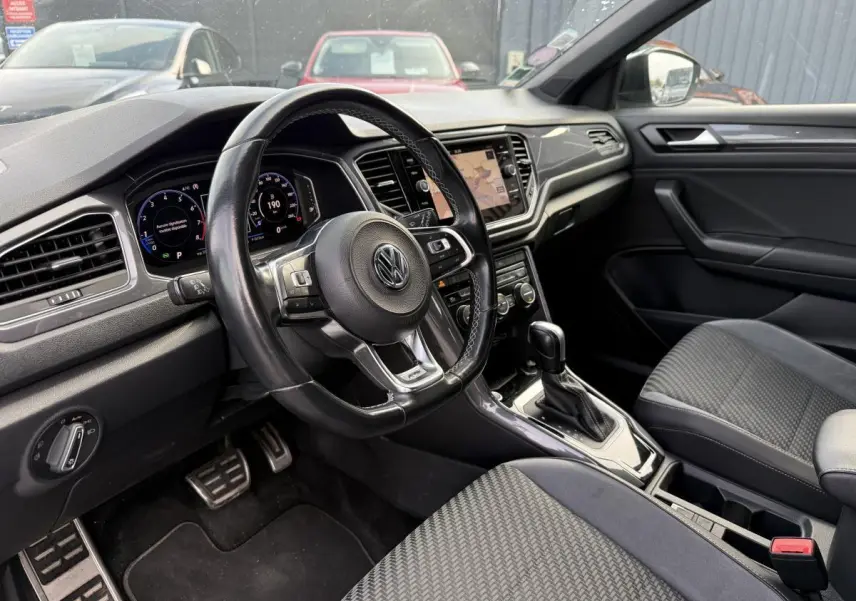 Intérieur avant du Volkswagen T-Roc 1.5 TSI gris, vue côté conducteur avec volant cuir et tableau de bord digital.