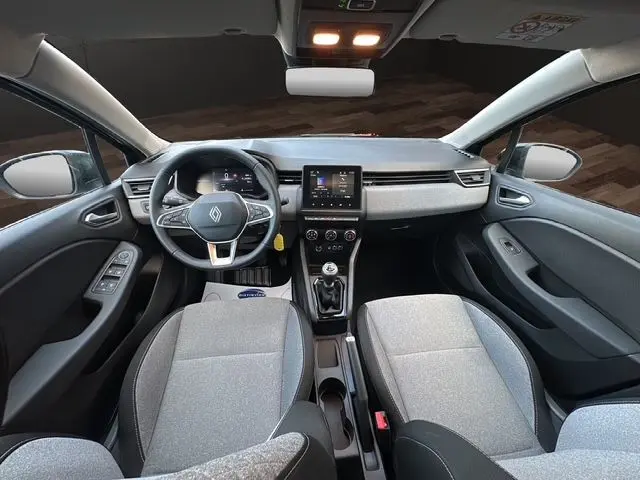 Vue intérieure avant de la Renault Clio V diesel 2025, avec tableau de bord moderne, volant multifonction et sièges tissu gris noir.