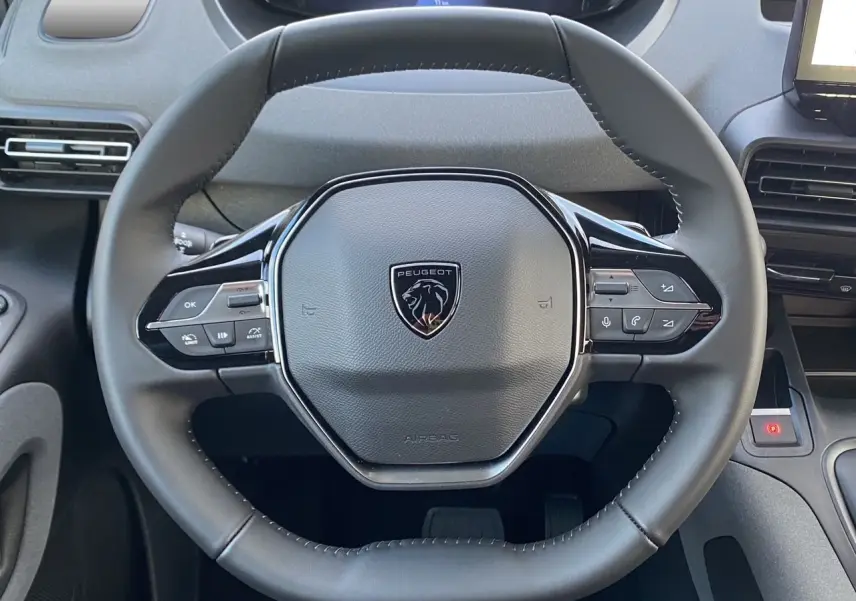 Vue rapprochée du volant cuir noir avec logo Peugeot du Rifter 2025, mettant en valeur les commandes multifonctions.