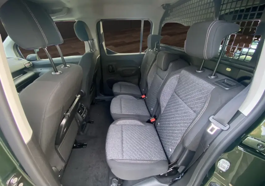 Vue intérieure côté droit du Peugeot Rifter 2025 vert Sirkka, montrant les sièges arrière en tissu gris avec grille de séparation.