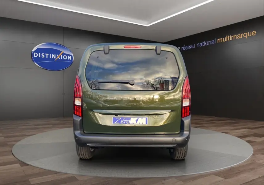 Vue arrière du Peugeot Rifter 2025 vert Sirkka avec hayon vitré et feux verticaux rouges en intérieur showroom.
