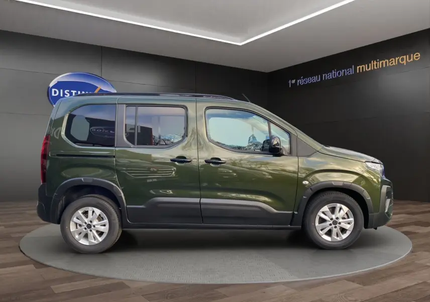 Profil droit du Peugeot Rifter 2025 vert Sirkka avec jantes alliage 16'' et barres de toit noires en showroom.
