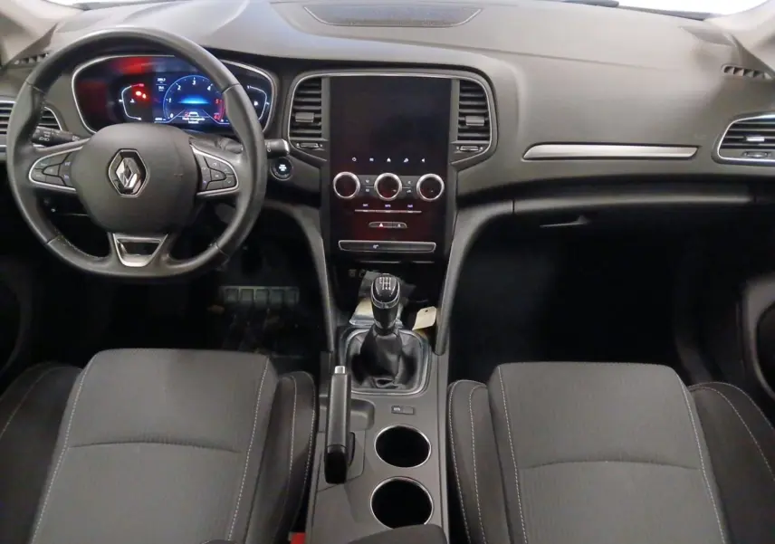 Vue intérieure frontale de la Renault Mégane IV 2020 avec tableau de bord noir, volant multifonction et boîte manuelle.