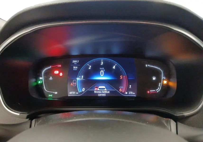 Vue rapprochée du tableau de bord numérique de la Renault Mégane IV blanche, affichant les compteurs et alertes.