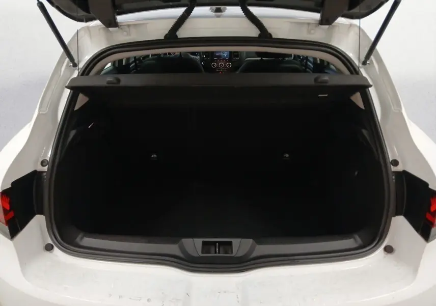 Coffre ouvert vu de l'arrière d'une Renault Mégane IV blanche, avec intérieur noir et tablette de coffre relevée.