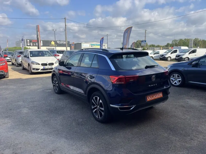Volkswagen T-Roc gris en 3/4 arrière droit sur un parking, avec badge "OCCASION" visible sur le coffre.