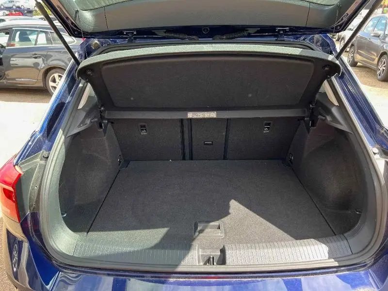 Coffre ouvert vu de l'arrière d'un Volkswagen T-Roc gris Urano, montrant un espace de chargement propre et spacieux.