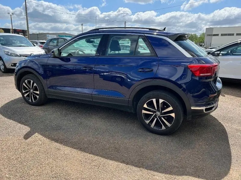 Profil droit d'un Volkswagen T-Roc 2020 bleu foncé avec toit noir et jantes alliage bicolores sur parking.