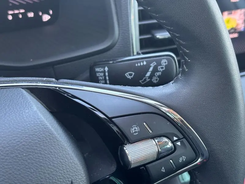 Gros plan sur les commandes du volant en cuir noir du Skoda Karoq blanc Lune métallisé, mettant en valeur la molette et les boutons multifonctions.