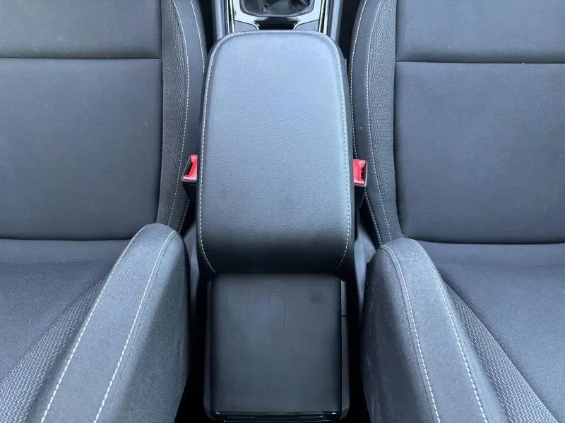 Vue plongeante sur l'accoudoir central noir entre les sièges avant en tissu noir du Skoda Karoq blanc Lune 2024.