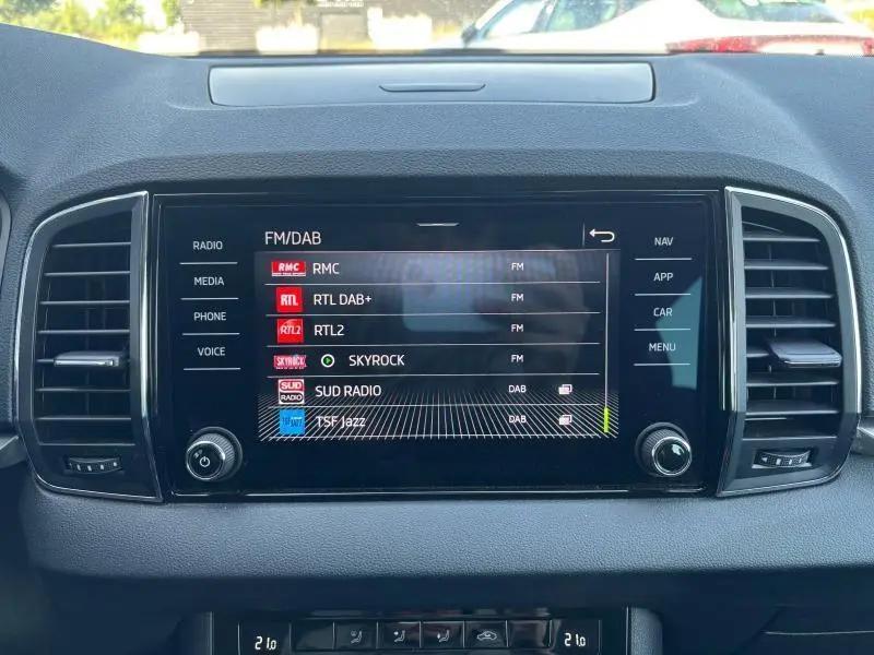 Écran tactile central du Skoda Karoq 2024 affichant les stations radio FM/DAB, entouré de grilles d'aération noires.
