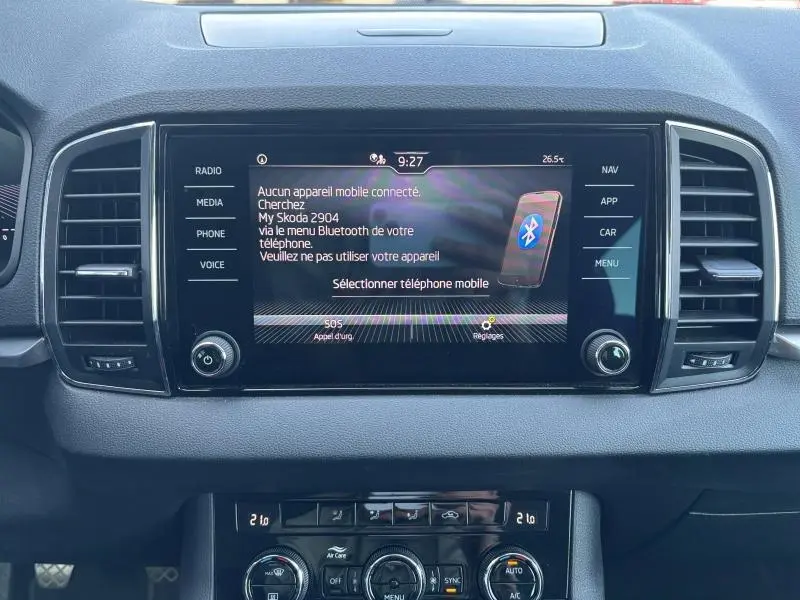 Tableau de bord du Skoda Karoq blanc, vue frontale centrée sur l'écran tactile multimédia et commandes climatisation.