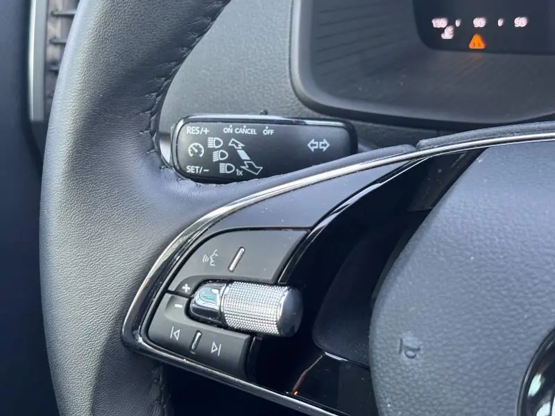 Gros plan sur les commandes vocales et volume au volant cuir noir du Skoda Karoq blanc Lune 2024, côté gauche.