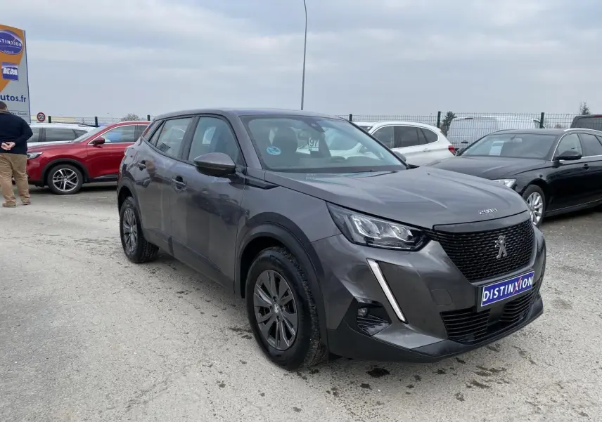 Peugeot 2008 gris foncé vue 3/4 avant droit sur parking avec calandre noire et feux LED griffés.