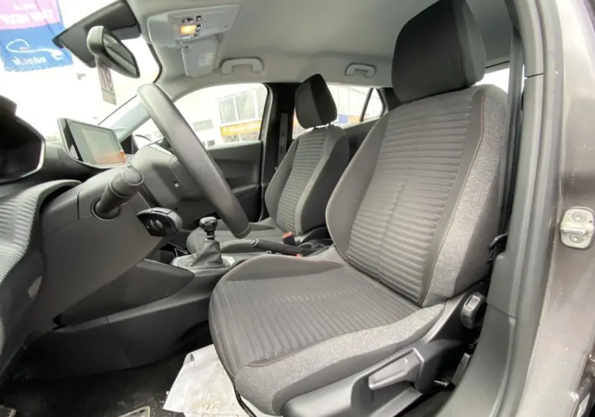 Intérieur avant droit du Peugeot 2008 gris foncé 2021, sièges tissu gris avec surpiqûres, volant et levier de vitesse manuels visibles.