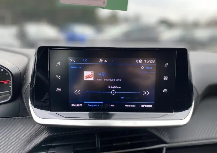 Écran tactile central du Peugeot 2008 2021 affichant la radio NRJ, avec tableau de bord en carbone gris foncé.