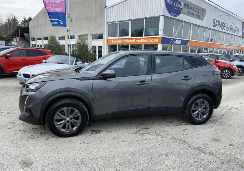 Profil côté gauche d'un Peugeot 2008 gris foncé métallisé garé devant un garage multimarque.