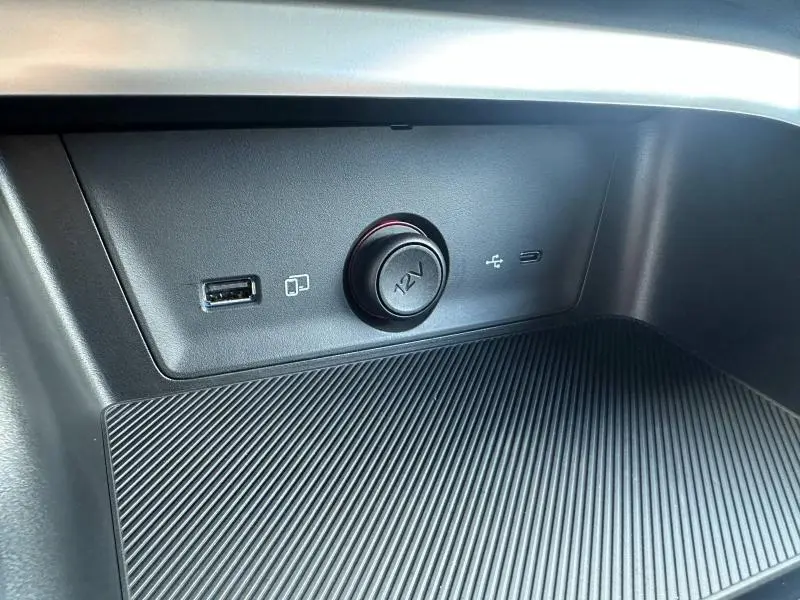 Gros plan sur la prise 12V et port USB intégrés dans la console centrale noire du MG ZS Hybrid+ 2025.