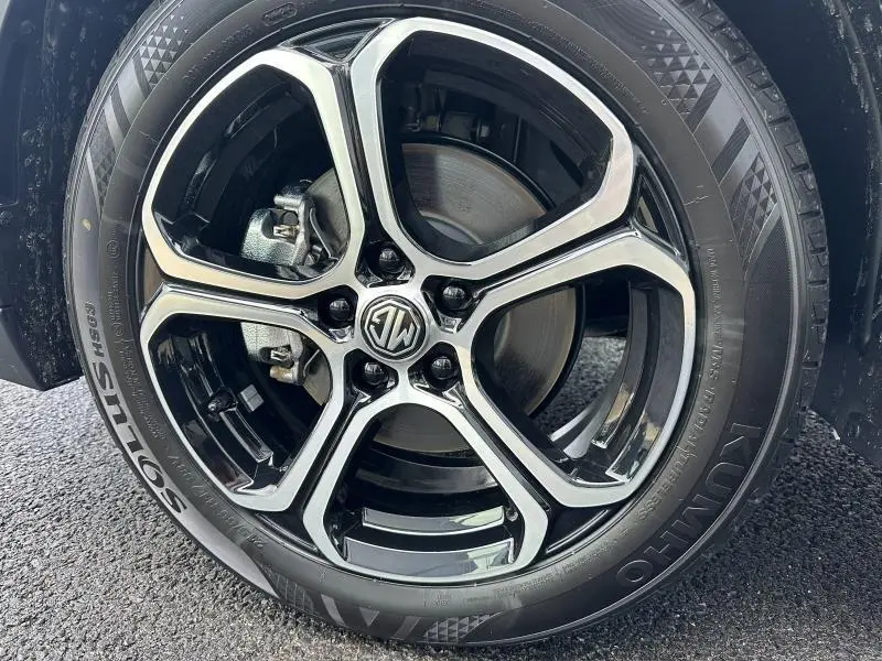 Gros plan sur la jante alliage noire et argentée avec logo MG du MG ZS Hybrid+ blanc, roue avant droite visible.