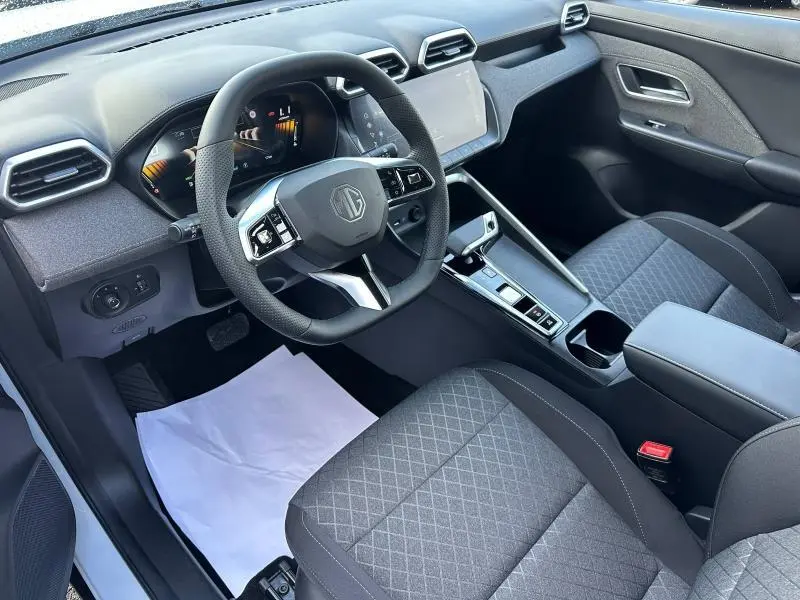 Vue intérieure côté conducteur du MG ZS Hybrid+ 2025, volant cuir multifonction et sièges tissu noir avec console centrale moderne.