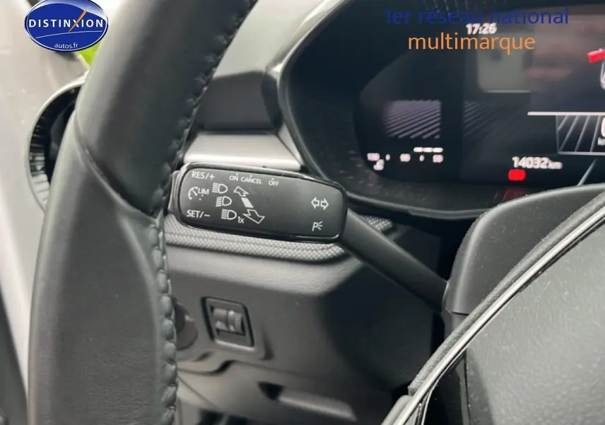 Gros plan sur la commande de régulateur de vitesse à gauche du volant cuir d'une Skoda Fabia blanche, tableau de bord numérique visible.