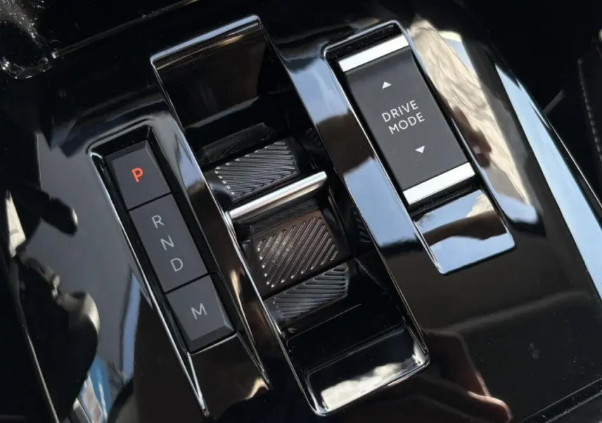 Gros plan sur la console centrale noire brillante de la Citroën C4 Hybrid 145 CH, avec sélecteur de vitesses automatique et bouton Drive Mode.