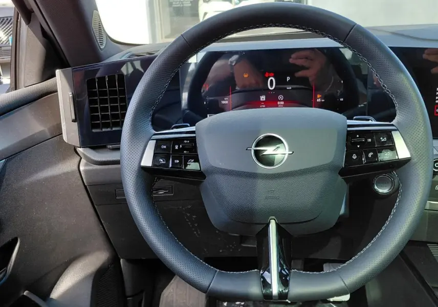 Vue intérieure centrée sur le volant cuir noir de l'Opel Astra 2025 avec tableau de bord digital et écran tactile.