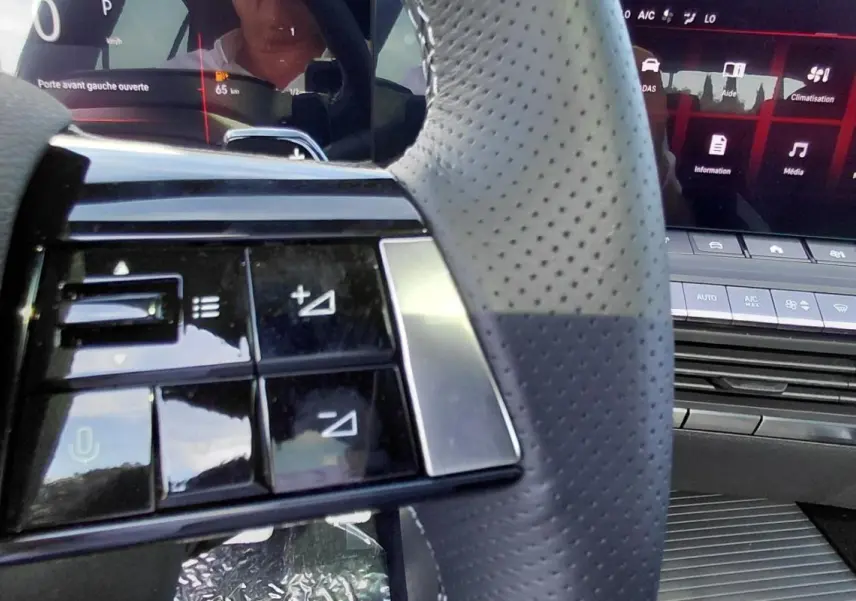 Gros plan sur les commandes au volant en cuir perforé de l’Opel Astra 2025, avec écran tactile et console centrale visible.