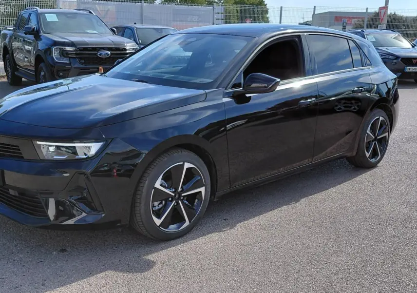 Opel Astra noire vue en 3/4 avant droit, vitres surteintées et jantes alliage 17 pouces distinctives.