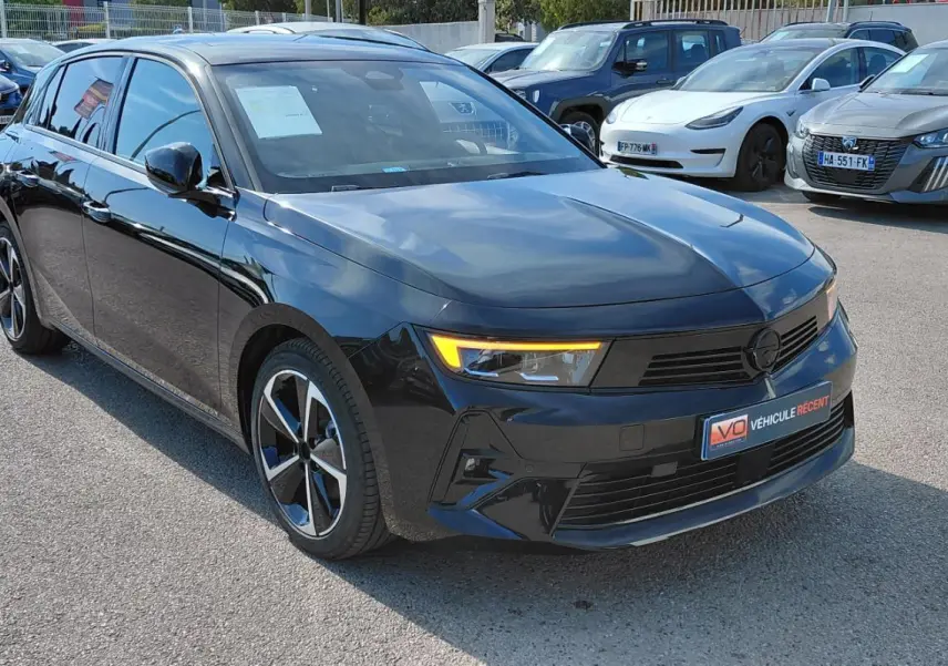 Opel Astra noire vue 3/4 avant droit, avec jantes alliage 17 pouces et feux diurnes allumés.