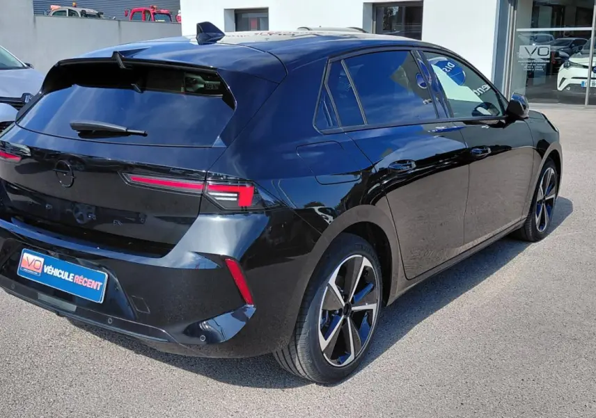 Opel Astra noire vue 3/4 arrière droit, jantes alliage 17 pouces et vitres surteintées en extérieur.
