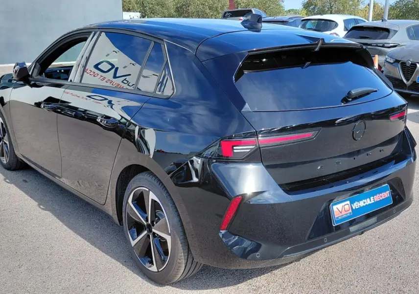 Opel Astra noire vue 3/4 arrière droit, avec jantes alliage 17 pouces et vitres surteintées.