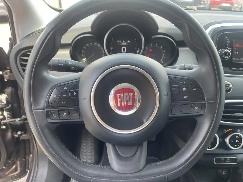 Volant multifonction noir avec logo FIAT rouge au centre, tableau de bord et commandes visibles dans un Fiat 500X 2015.