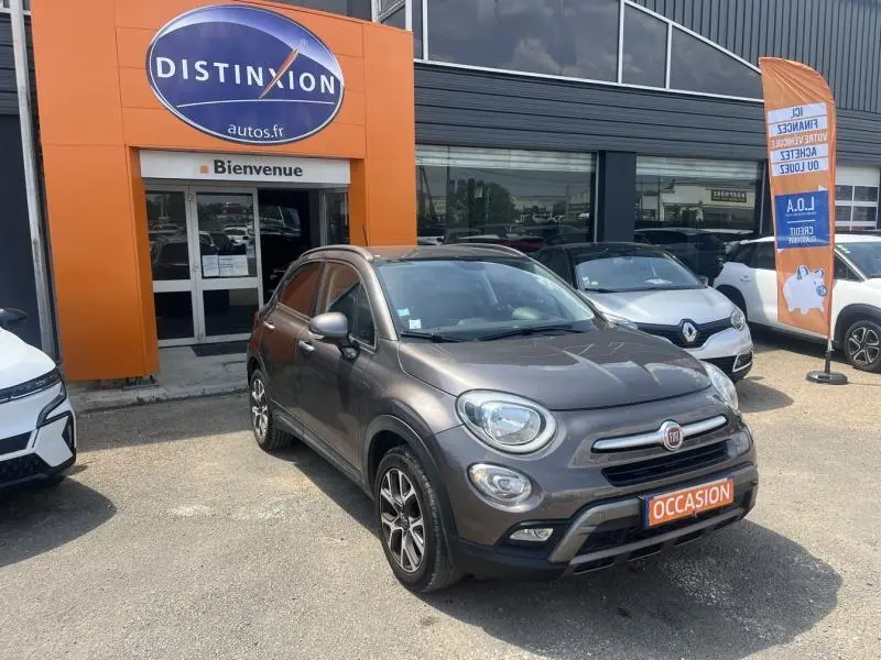 Vue 3/4 avant d'une FIAT 500X bronze métallisé stationnée devant un concessionnaire avec plaque "OCCASION" visible.