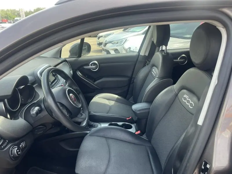 Intérieur avant du FIAT 500X bronze Magnetico, sièges noirs avec logo 500 brodé et volant multifonction visible.