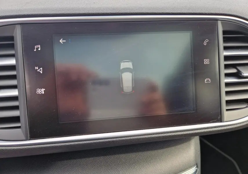 Écran central tactile de la Peugeot 308 gris artense montrant l'aide au stationnement avec vue du dessus du véhicule.