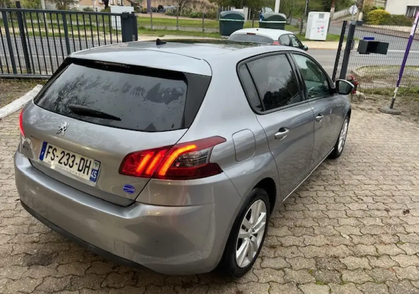 Vue 3/4 arrière droite d'une Peugeot 308 gris artense avec feux arrière allumés et vitres teintées.