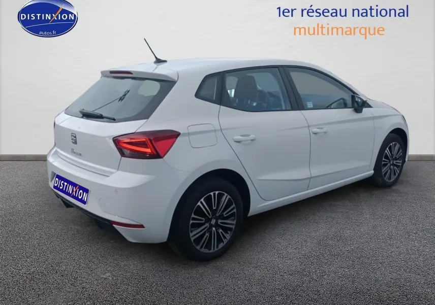 Vue 3/4 arrière droite d'une SEAT Ibiza blanche Nevada avec jantes alliage et feux arrière allumés.