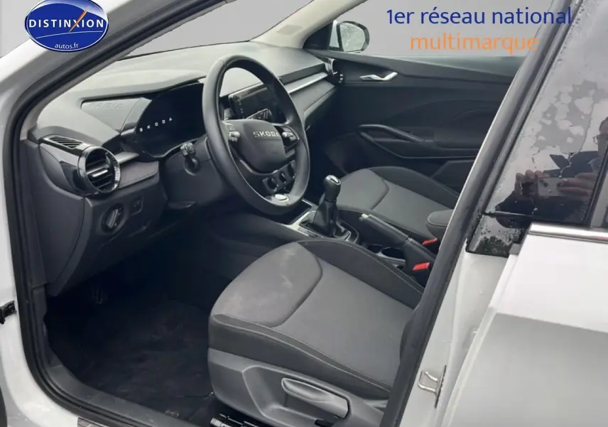 Vue intérieure côté conducteur d'une Skoda Fabia blanche 2025, avec volant cuir et boîte manuelle visible.