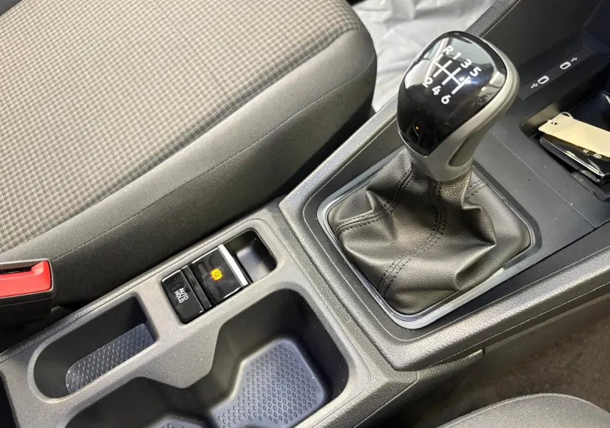 Gros plan sur la console centrale du Volkswagen Caddy 2025 gris argent, mettant en valeur le levier de vitesses manuel et le frein à main électronique.