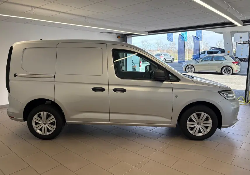 Volkswagen Caddy 2025 gris argent vu de profil côté gauche dans un showroom lumineux.