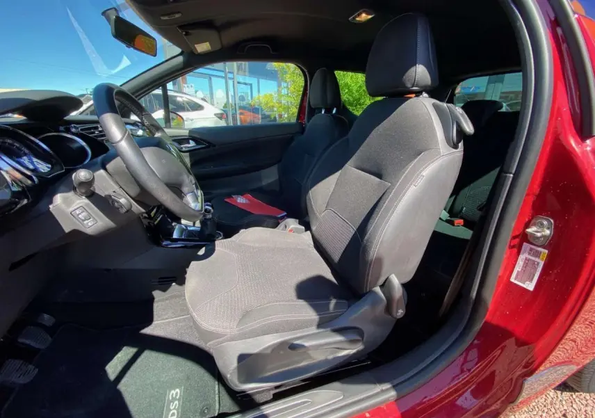 Vue intérieure côté conducteur d'une DS3 rouge avec sièges tissu gris et tableau de bord noir lumineux.