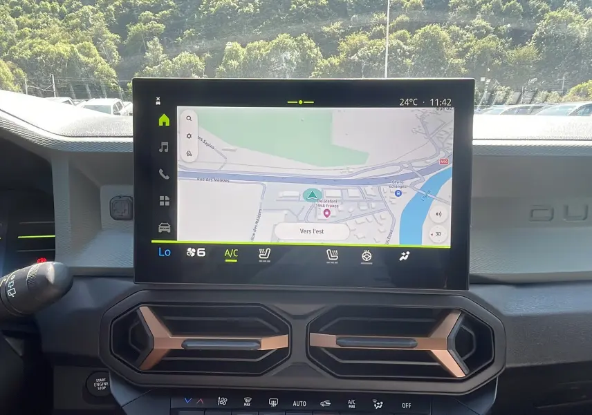 Vue intérieure du tableau de bord du Dacia Duster 2025 avec écran tactile central affichant la navigation et aérateurs hexagonaux.