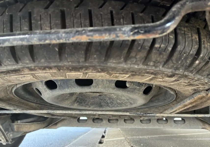 Vue en contre-plongée du pneu de secours sous un Renault Trafic Fourgon blanc, montrant la roue de secours et le châssis inférieur.